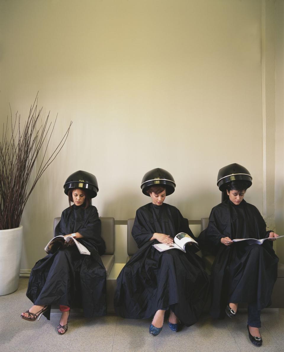 ladies at salon under hair dryers reading magazine