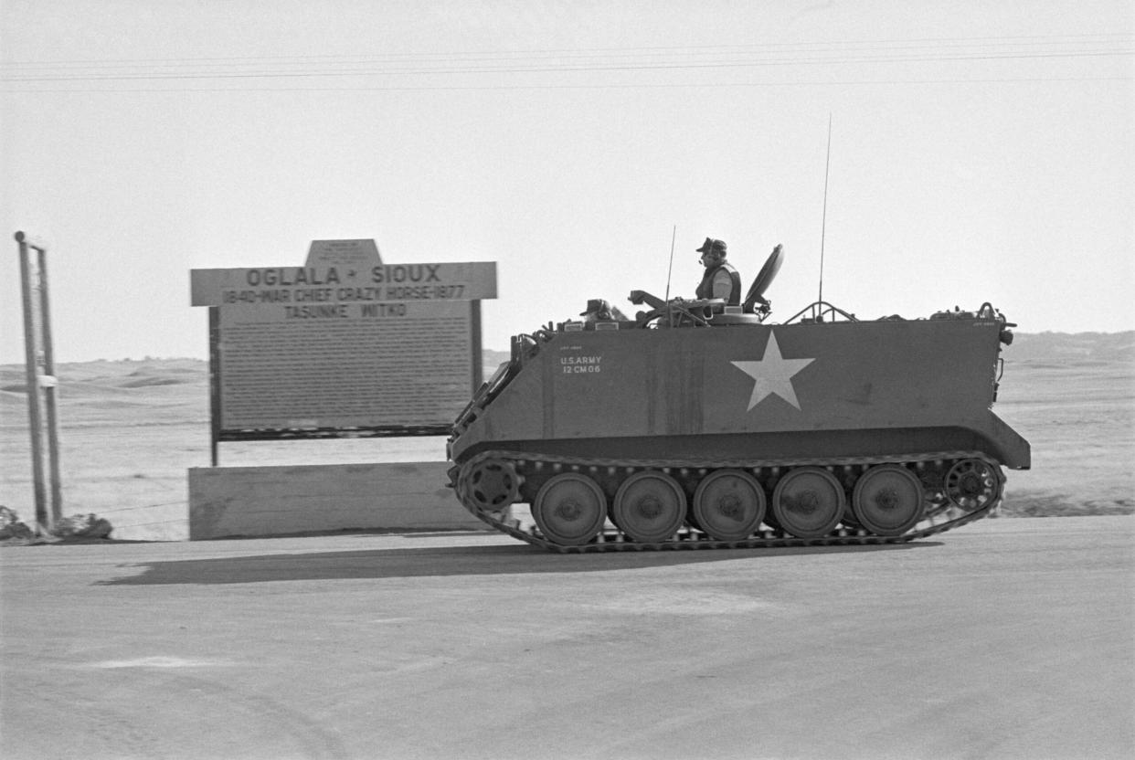 Wounded Knee, SD, 1973: an armored personal carrier passes a historic marker commemorating Oglala Sioux war chief Crazy Horse, and helps seal off the Wounded Knee area held by the American Indian Movement. (Credit: Getty Images).