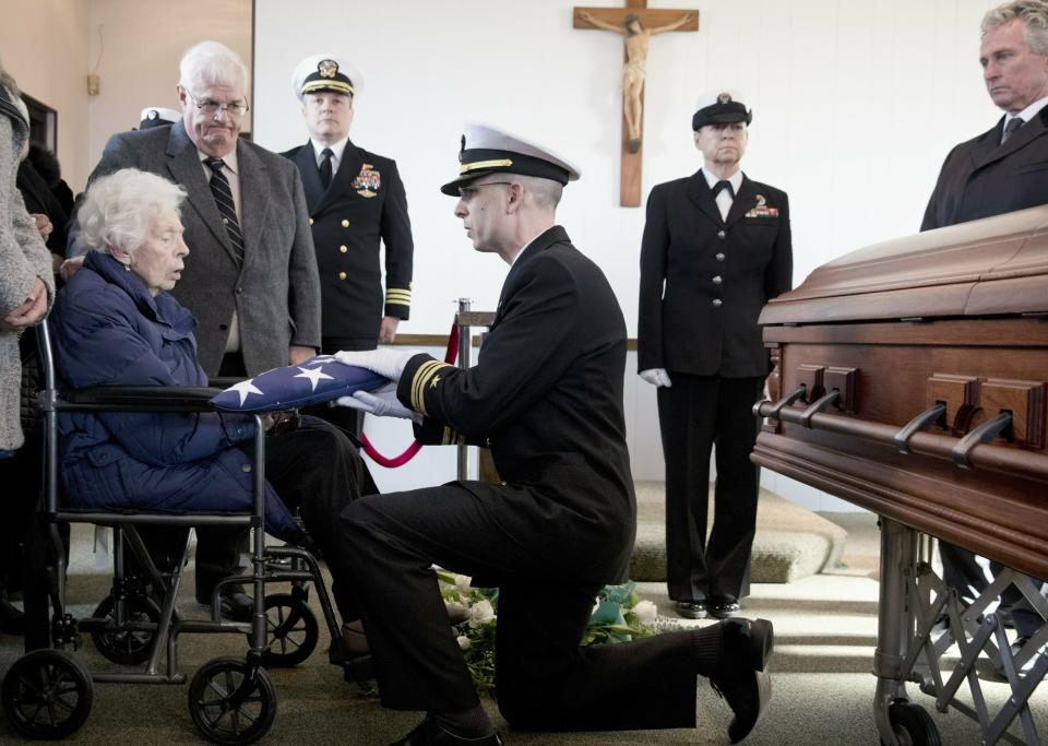 Rita Mendonsa, left, receives the flag that draped her husband George's casket during funeral services at St. Columba Cemetery in Middletown, R.I., Friday, Feb. 22, 2019. George Mendonsa, the sailor sailor photographed kissing a woman in Times Square in New York at the end of World War, died Sunday at age 95. (AP Photo/Michael Dwyer)