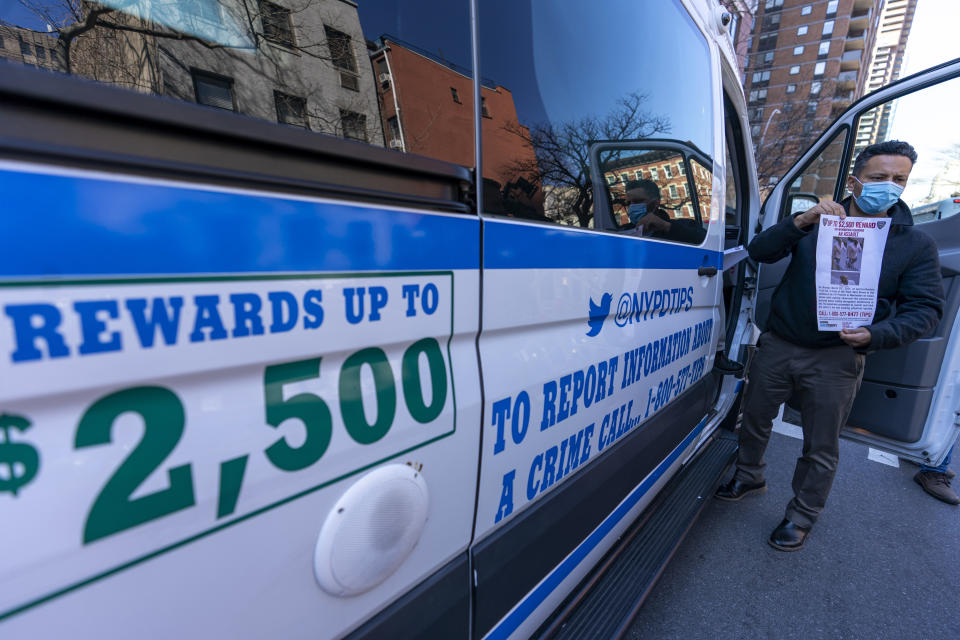 A police officer holds a sign near the crime scene offering a reward for information on the person who attacked an Asian American woman, Tuesday, March 30, 2021, in New York. The New York City Police Department says an Asian American woman was attacked by a man Monday afternoon who repeatedly kicked her in front of witnesses who seemingly stood by. (AP Photo/Mary Altaffer)