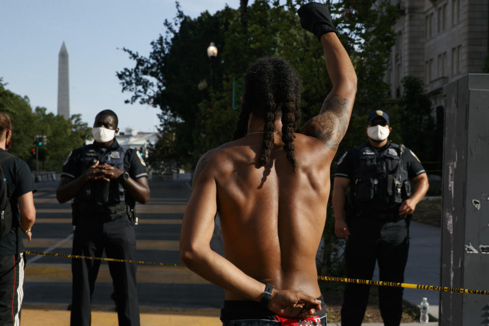 FILE - In this June 24, 2020, file photo Aaron Covington of St. Louis, center, holds his fist up as he faces a police line while leading people in a chant as demonstrators protest in front of a police line on a section of 16th Street that's been renamed Black Lives Matter Plaza in Washington. An activist collective led by Black Lives Matter is trying to capitalize on shifting public opinion, and the demands include major cuts in funding for the Metropolitan Police Department. The District of Columbia Council had indicated it would push for up to $15 million in cuts, but District of Columbia Mayor Muriel Bowser is defending her 2021 budget proposal, which includes a 3.3% increase in police money. (AP Photo/Jacquelyn Martin, File)