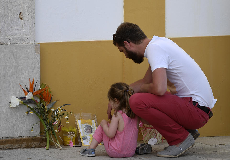 A man and a little girl look at flowers, candles and a photograph of "Maddie", placed on the street as a tribute to missing child Madeleine McCann, outside the church in Praia da Luz near Lagos on May 3, 2017 on the 10th anniversary of her disappearance. Madeleine McCann (Maddie) disappeared in Praia da Luz on May 3, 2007. Portuguese police closed the case in 2008 before reopening it five years later. / AFP PHOTO / FRANCISCO LEONG        (Photo credit should read FRANCISCO LEONG/AFP/Getty Images)