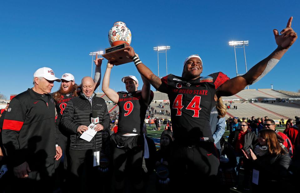 San Diego State linebacker Kyahva Tezino (44), quarterback Ryan Agnew (9), tight end Parker Houston, second from left, and coach Rocky Long, left, celebrate with the trophy after beating Central Michigan in the New Mexico Bowl, Saturday, Dec. 21, 2019 in Albuquerque.