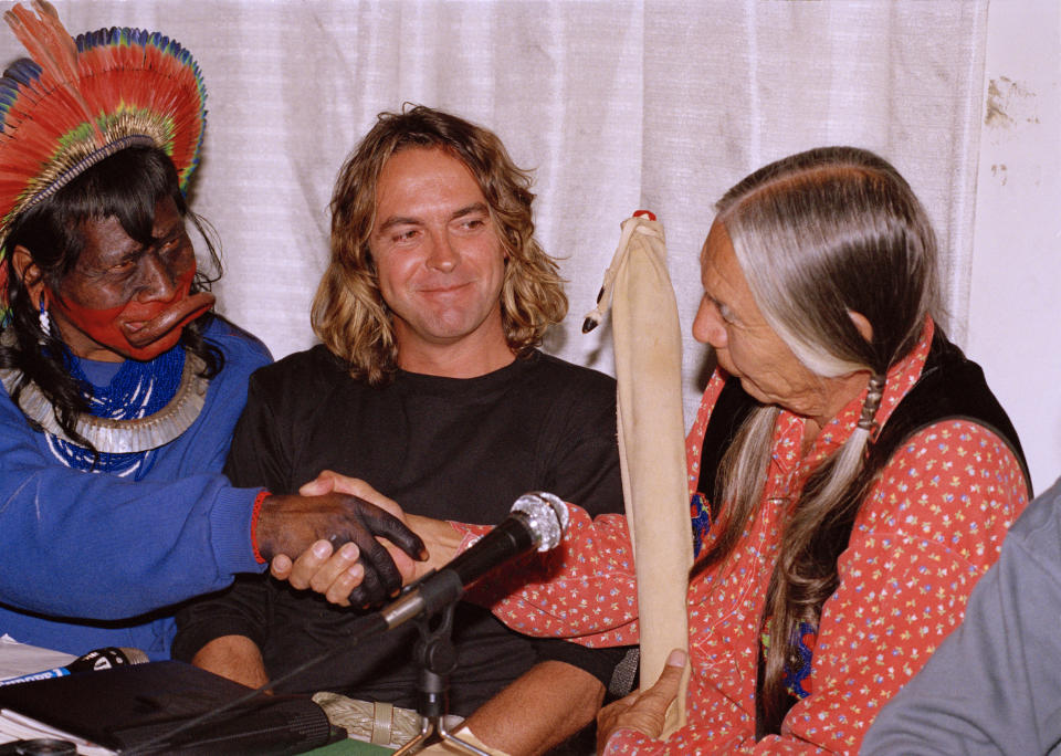 FILE - Chief Raoni, left, of the Indigenous Kayapo Nation in Brazil, left, and Native American Indian Red Crow, right, of South Dakota, shake hands during a press conference to present a project for an environmental park in Brazil's Amazon, as Belgian filmmaker Jean-Pierre Dutilleux, who is participating in the project, sits between them, in Paris, France, April 13, 1989. For five decades, the Amazonian tribal chief Raoni and Belgian film director enlisted presidents and royals, even Pope Francis, to improve the lives of Brazil’s Indigenous peoples and protect their lands. Behind the scenes, however, the relationship was nearing its end. Not long after returning to Brazil in May 2024, the chief of the Kayapo severed ties with his Belgian acolyte. (AP Photo/Pierre Gleizes, File)