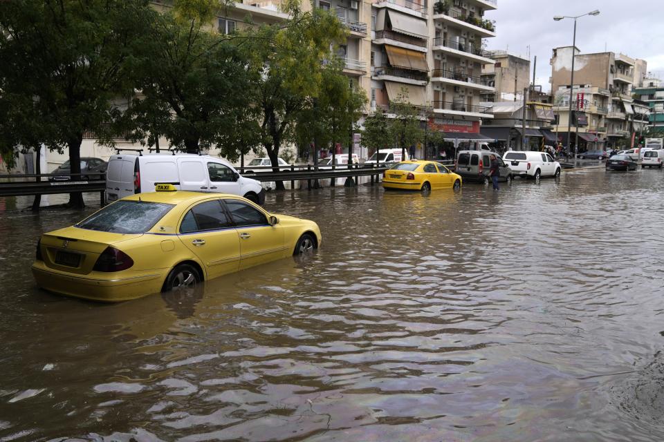 A taxi is stranded as other vehicles cross a flooded avenue in Athens, Thursday, Oct. 14, 2021. Storms battered the Greek capital and other parts of southern Greece, causing traffic disruption and some road closures. (AP Photo/Thanassis Stavrakis)