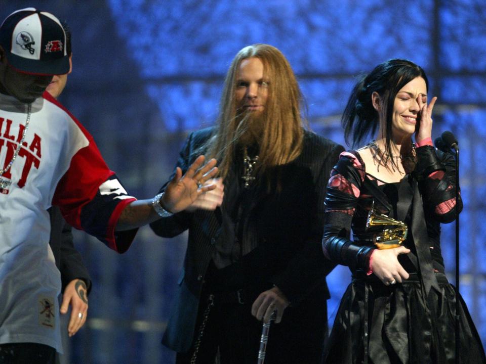 50 Cent in a jersey and baseball cap with his hands off walking off stage with the band and lead singer Amy Lee holding the award with the other hand up to her face while in disbelief and smiling.