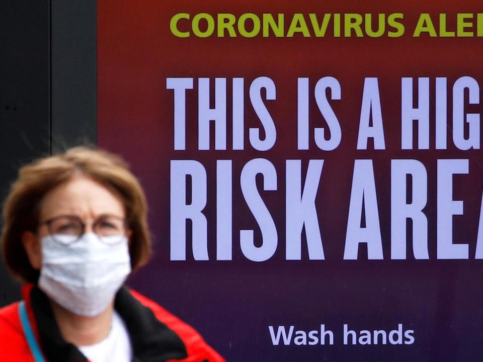 A woman wearing a protective mask walks past a warning sign in Manchester: REUTERS