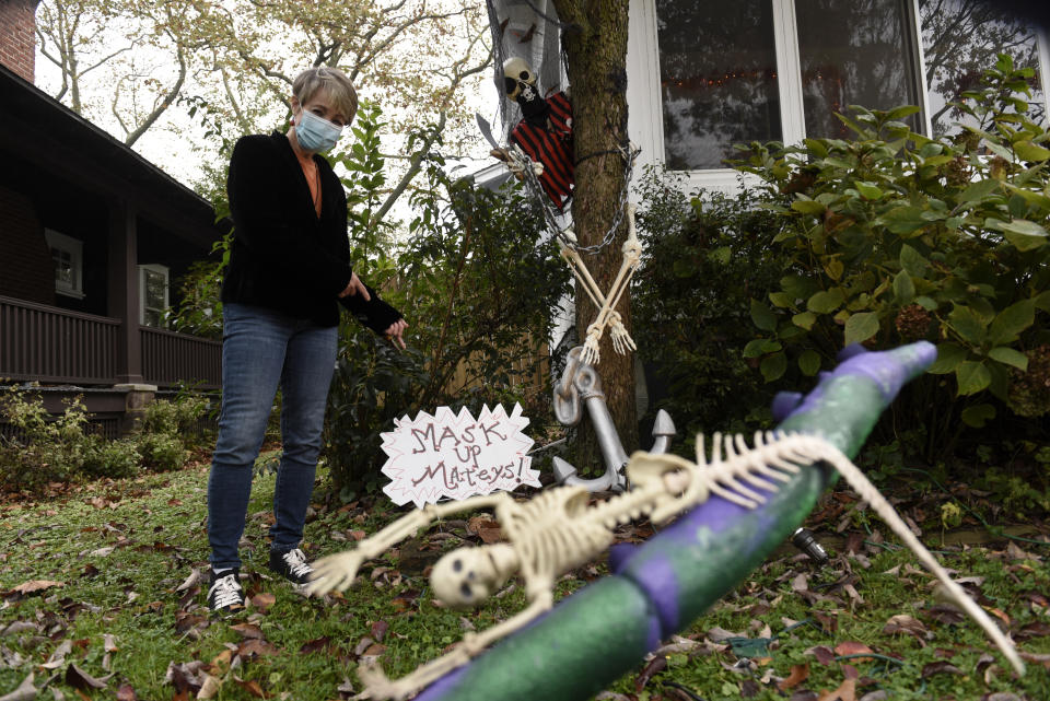 Carol McCarthy poses next to pirate-themed Halloween decorations reminding people to mask up while trick-or-treating during the COVID-19 pandemic, Monday, Oct. 26, 2020, in Palmyra, N.J. (AP Photo/Michael Perez)