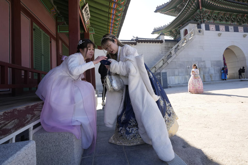 Hong Kong travelers wearing South Korean traditional "Hanbok" costume watch a smartphone at the Gyeongbok Palace, the main royal palace during the Joseon Dynasty, and one of South Korea's well known landmarks in Seoul, South Korea, on Jan. 18, 2023. The expected resumption of group tours from China is likely to bring far more visitors. (AP Photo/Ahn Young-joon)