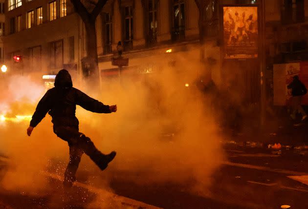 A masked demonstrator kicks an object amid clashes with riot police in Paris
