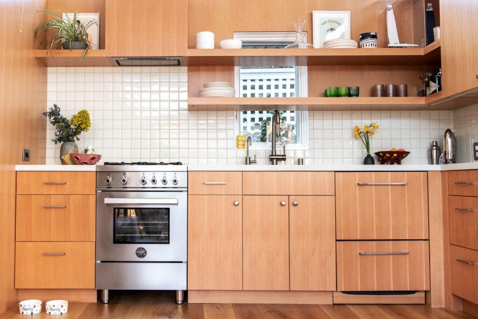 A tiny kitchen with natural wood cabinets and white tile.