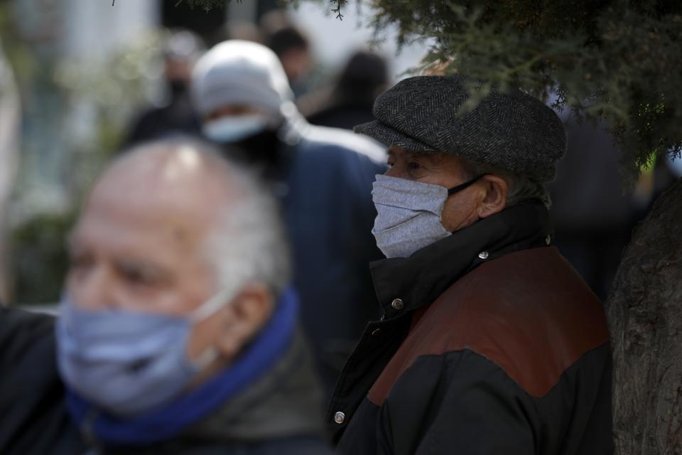 A man wearing a face mask against the spread of coronavirus, stands under a tree as others wait in a queue to conduct rapid tests for the COVID-19 in Athens, Wednesday, March 3, 2021. Greece has recorded a new spike in COVID-19 infections, nearly half of which were recorded in the greater Athens region where hospital intensive care units are quickly filling up. (AP Photo/Thanassis Stavrakis)