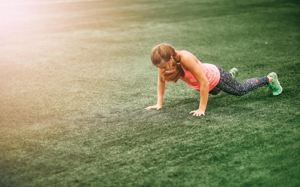 Fit woman in bright sports clothes to do burpees on the green grass - Alamy Stock Photo