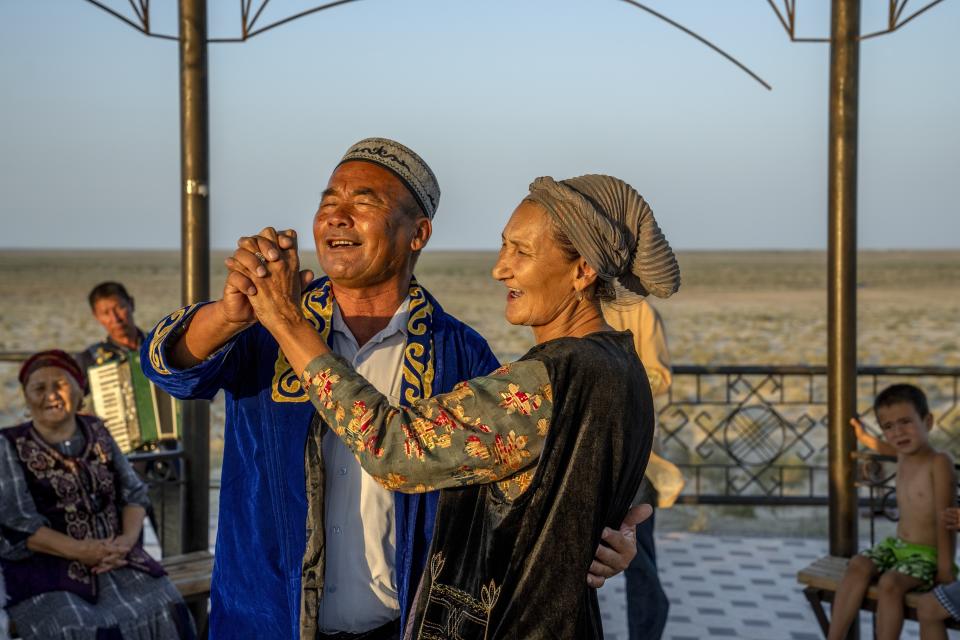 A man and woman dance next to a sand lot filled with ships formerly used on the Aral Sea in Muynak, Uzbekistan, Tuesday, July 11, 2023. (AP Photo/Ebrahim Noroozi)