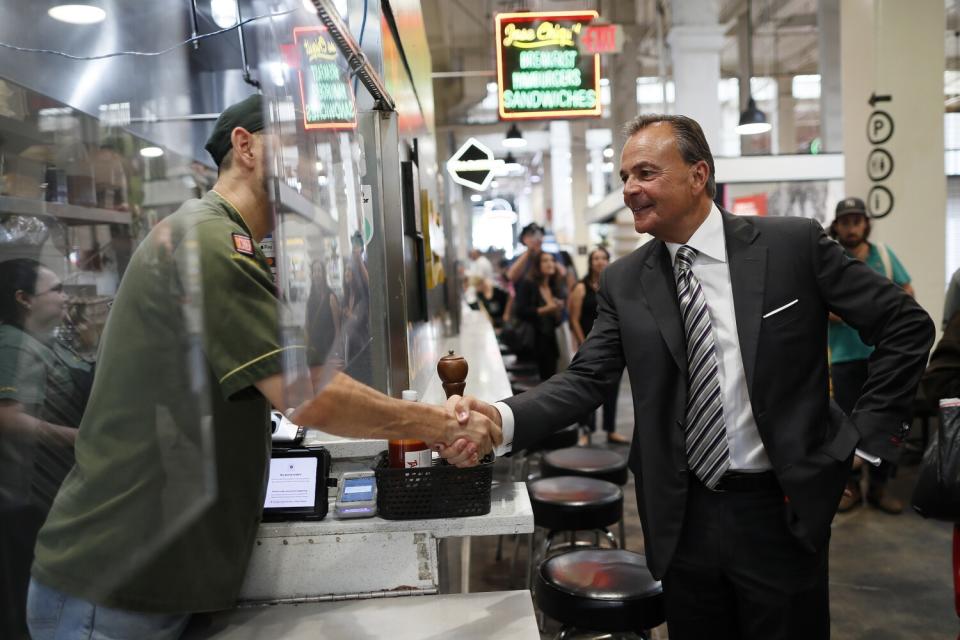 Rick Caruso shakes hands with a man behind a counter.