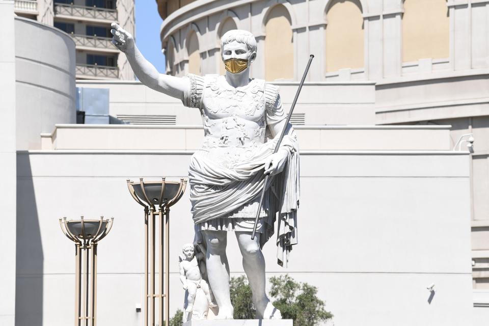 The Caesar statue at the entrance to Caesars Palace sports a gold mask as the hotel casinos reopen after a 2 1/2-month shutdown.