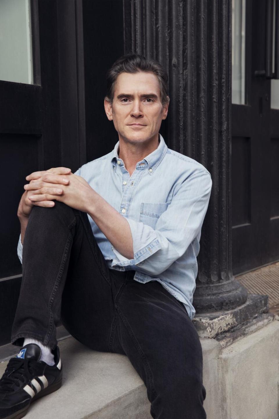 Billy Crudup sits on a ledge outside for a portrait.