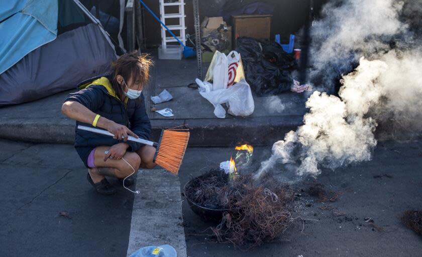 Los Angeles, CA - December 09: Toxic smoke billows up over a line of tents on the sidewalk as a person burns the plastic off copper wires in skidrow on Friday, Dec. 9, 2022, in Los Angeles, CA. They were using a broom the fan the flames. (Francine Orr / Los Angeles Times)