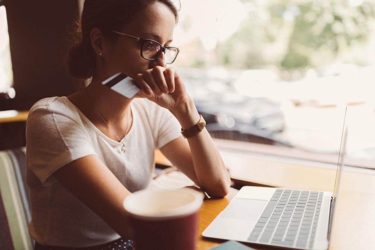 concerned woman looking at laptop with credit card, at cafe