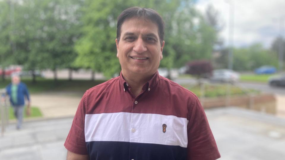 Mukesh Chugh is standing outside and smiling into the camera. he is wearing a red, white, and navy shirt 