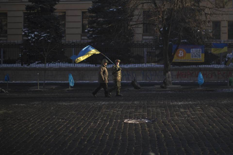 Opposition supporters, one of them holding a Ukrainian flag, walk along a street heading to Kiev's Independence Square, the epicenter of the country's current unrest, Ukraine, Monday, Feb. 3, 2014. Ukraine's president will return Monday from a short sick leave that had sparked a guessing game he was taking himself out of action in preparation to step down or for a crackdown on widespread anti-government protests. (AP Photo/Emilio Morenatti)