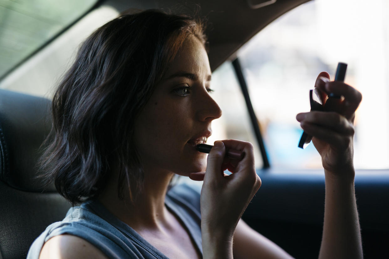 Portrait of young woman applying make up inside of a cab