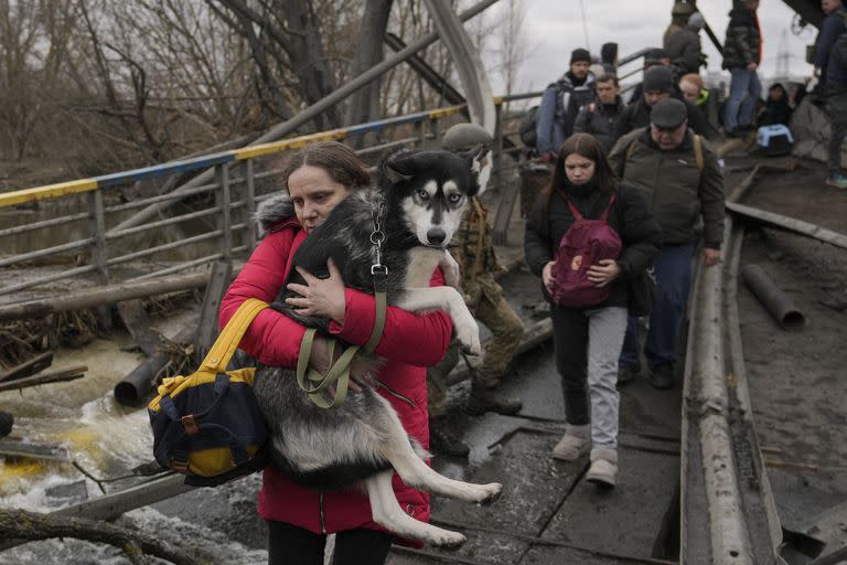 Una mujer carga a su perro mientras cruzan el río Irpín por un puente improvisado para huir de la violencia en Ucrania, el 5 de marzo de 2022