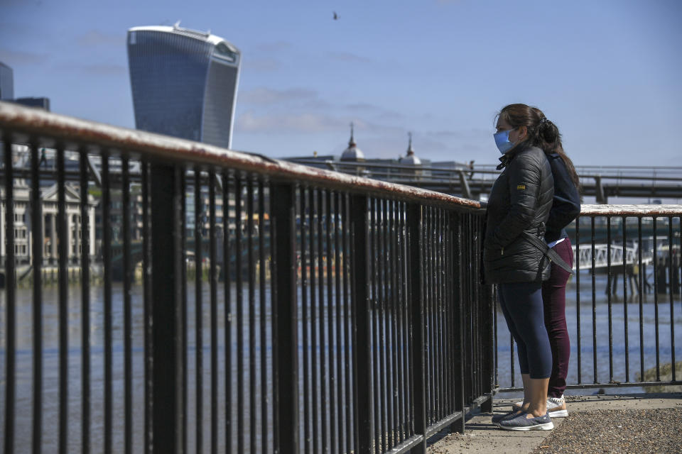 Two women wear protective masks on the south bank of the river Thames, as the lockdown due to the coronavirus outbreak continues, in London, Saturday, April 25, 2020.(AP Photo/Alberto Pezzali)