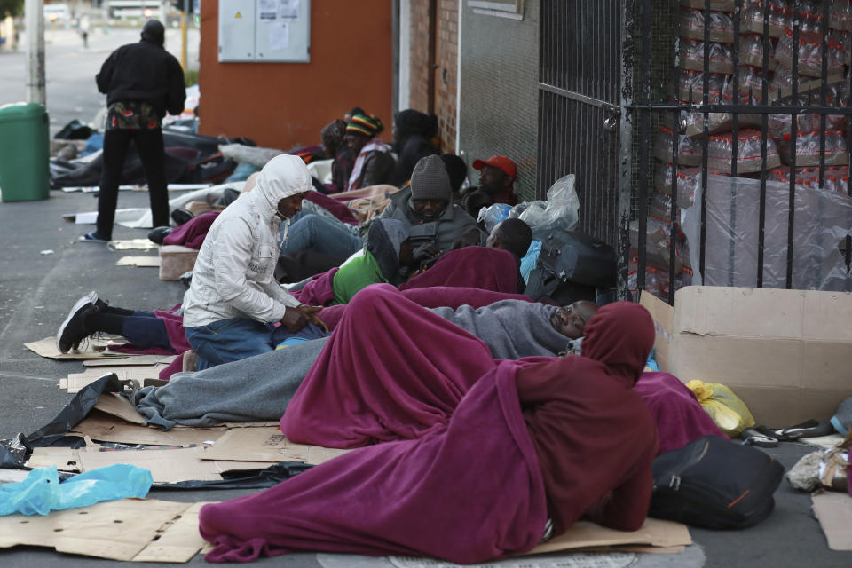 Refugees sleep on a sidewalk in Cape Town, South Africa, Friday, March 27, 2020, after South Africa went into a nationwide lockdown for 21 days in an effort to mitigate the spread to the coronavirus. The new coronavirus causes mild or moderate symptoms for most people, but for some, especially older adults and people with existing health problems, it can cause more severe illness or death. (AP Photo/Nardus Engelbrecht)