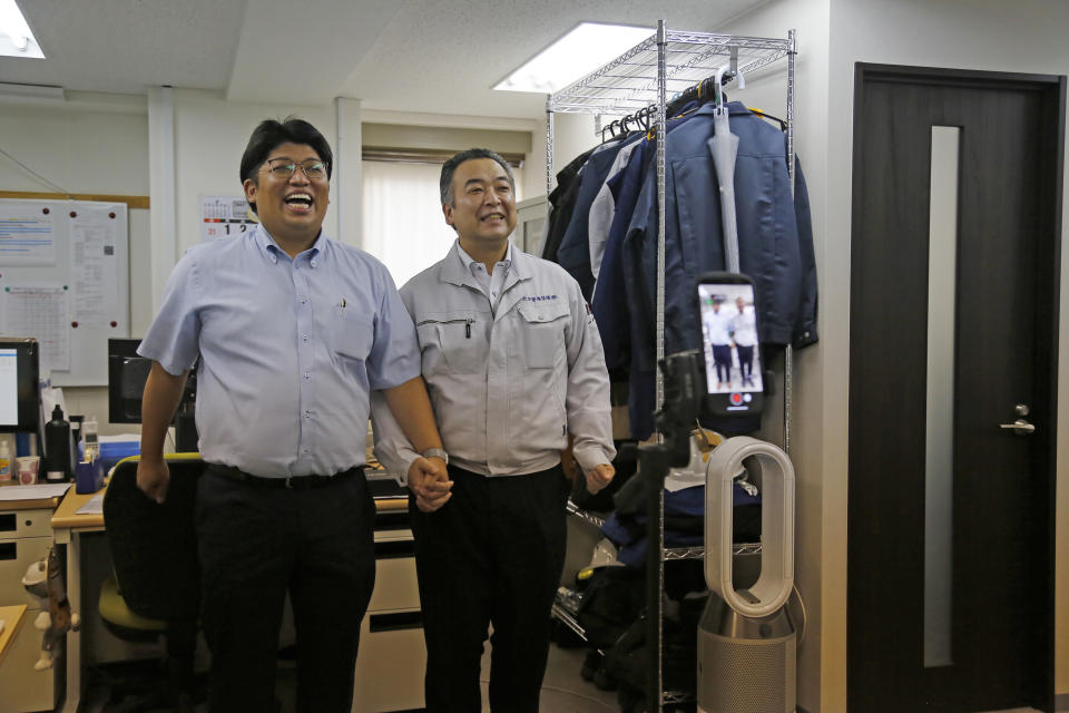 Daikyo Security Chief Executive Daisuke Sakurai, left, and General Manager Tomohiko Kojima take a Tik Tok video together as seen on the screen in the device (right) at the Tokyo headquarters office of Daikyo Security Co. in Tokyo Monday, Aug. 22, 2022. They’re your run-of-the-mill Japanese “salarymen,” but the chief executive and general manager at a tiny Japanese security company are among the nation’s biggest TikTok stars, drawing 2.7 million followers and 54 million likes, and honored with awards as a trend-setter on the video-sharing app. (AP Photo/Yuri Kageyama)