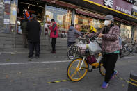 A resident wearing a mask pushes a bicycle with her groceries past a store controlling the flow of shoppers in Beijing, Friday, Nov. 25, 2022. Residents of China's capital were emptying supermarket shelves and overwhelming delivery apps Friday as the city government ordered accelerated construction of COVID-19 quarantine centers and field hospitals. (AP Photo/Ng Han Guan)