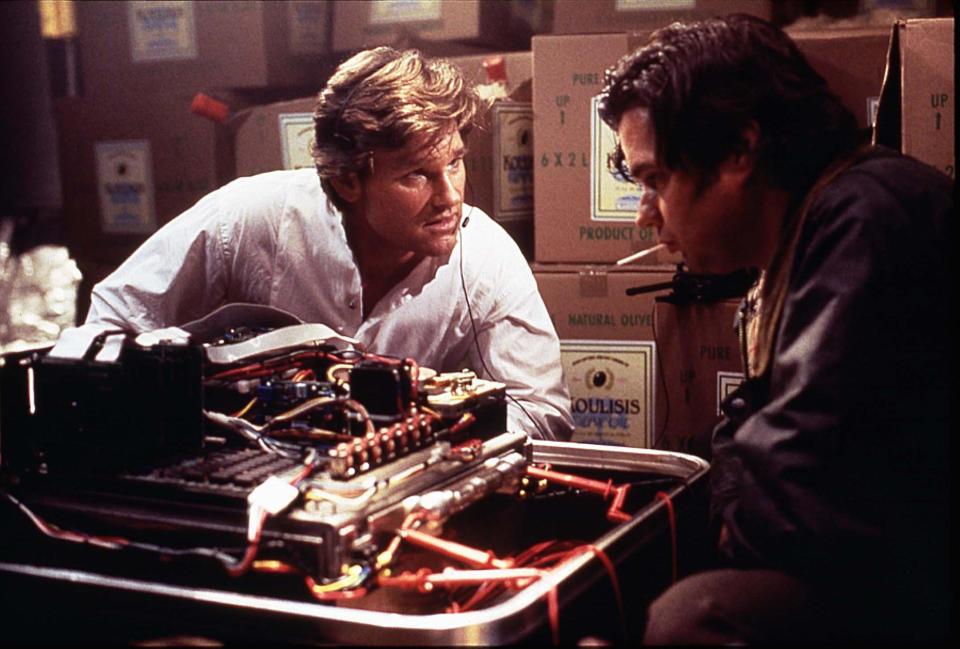 Kurt Russell talks with Oliver Platt near a mechanical device