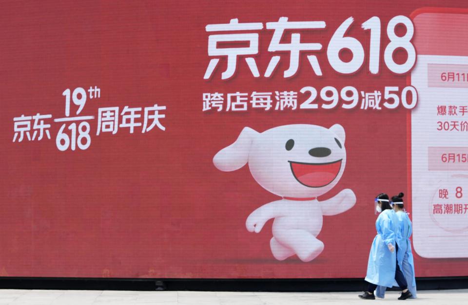 People wearing gear to protect against the novel coronavirus walk by a large screen showing an advertisement for the Chinese 618 online shopping festival on June 18, in Beijing. - Credit: Kyodo/AP