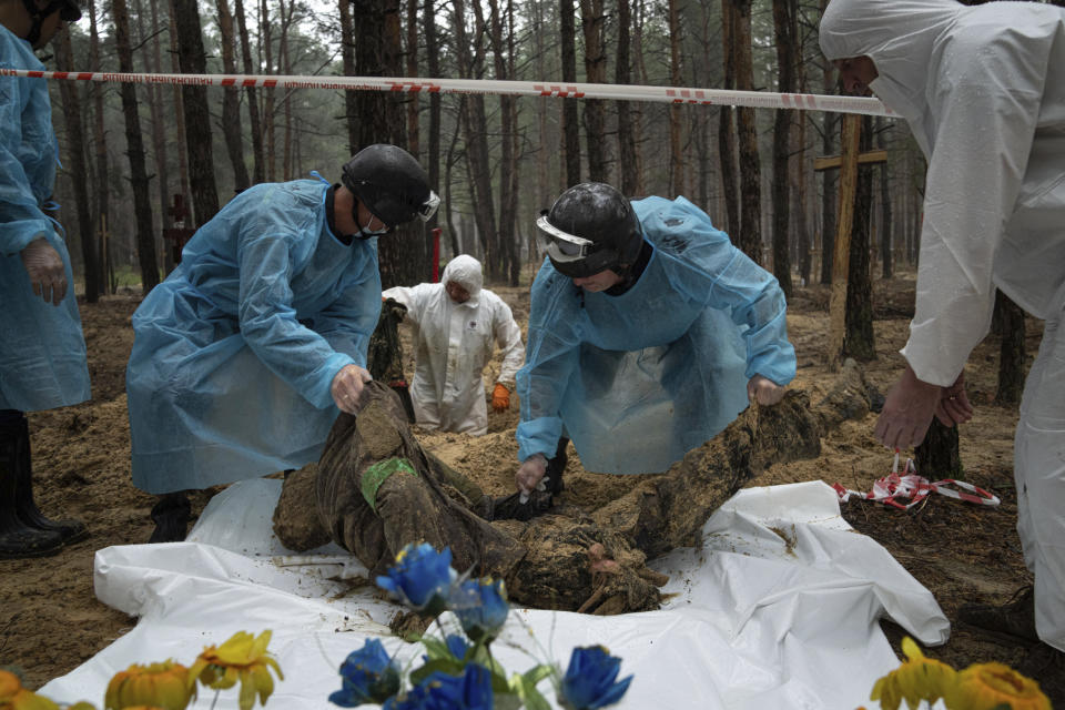 Emergency workers move the body of a Ukrainian soldier during the exhumation in the recently retaken area of Izium, Ukraine, Friday, Sept. 16, 2022. Ukrainian authorities discovered a mass burial site near the recaptured city of Izium that contained hundreds of graves. It was not clear who was buried in many of the plots or how all of them died, though witnesses and a Ukrainian investigator said some were shot and others were killed by artillery fire, mines or airstrikes. (AP Photo/Evgeniy Maloletka)