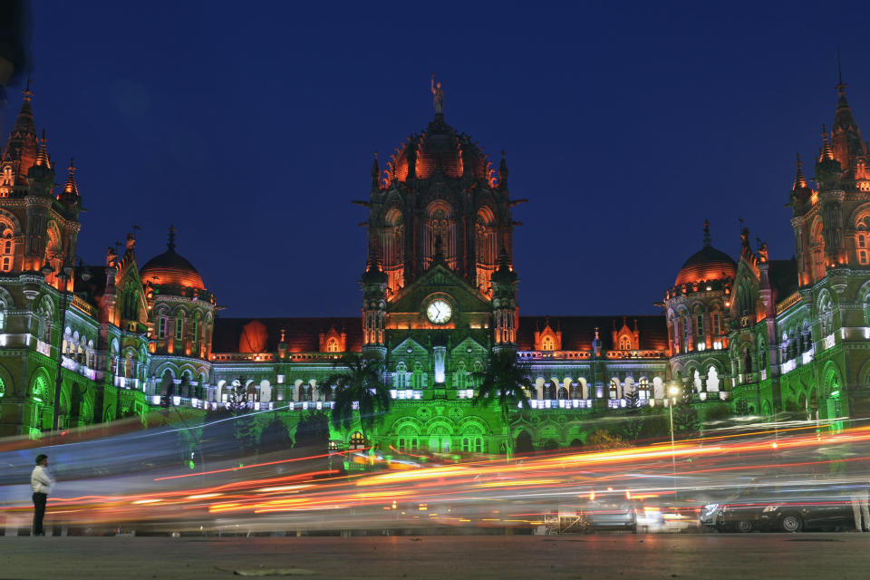 A man stands in front of the Chhatrapati Shivaji Maharaj train terminus building that is illuminated in the colors of the Indian national flag on the eve of the Republic Day in Mumbai, India, Thursday, Jan. 25, 2024. (AP Photo/Rajanish Kakade)