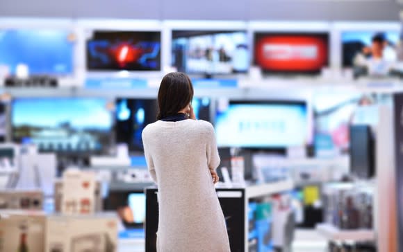 Woman staring at wall of televisions in electronics store