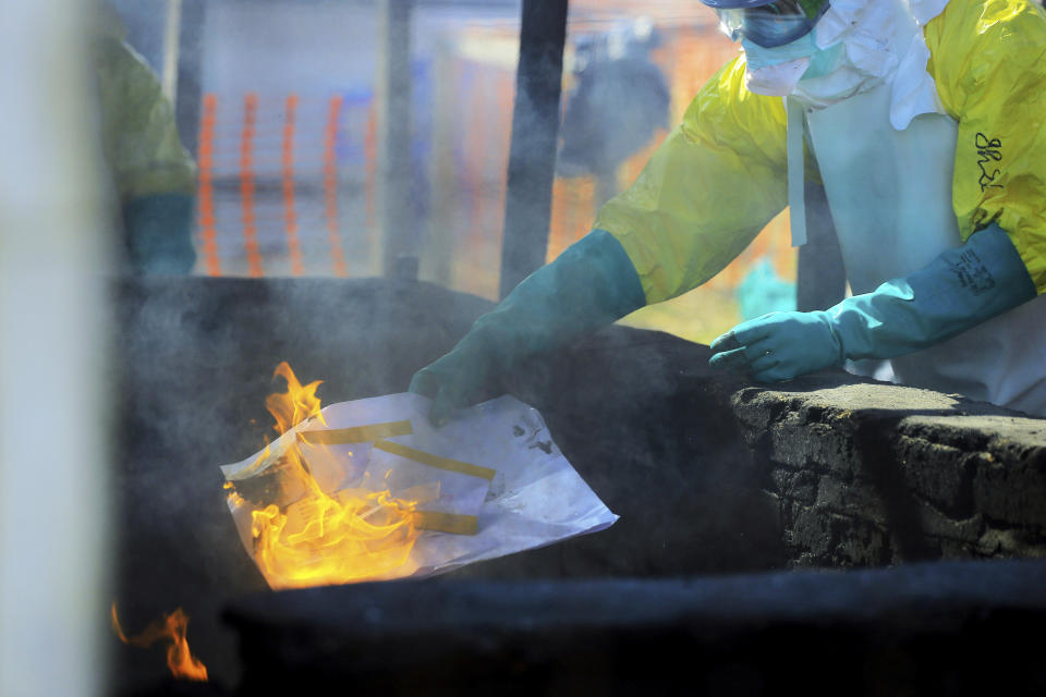 In this Saturday, July 20, 2019 photo, a health worker in protective clothing burns the college entry exam papers completed by Ebola patient Claude Mabowa Sasi, 21, after they were photographed for scoring in Beni, Congo. “I have not lost everything, and I am confident that I will succeed and honor my mother's memory,” Mabowa said. “If she were still here, I think she’d be proud of me.” (AP Photo/Al-Hadji Kudra Maliro)