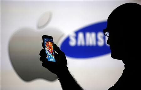 A man is silhouetted against a video screen with Apple and Samsung logos as he poses with a Samsung Galaxy S4 in this photo illustration taken in the central Bosnian town of Zenica, in this August 14, 2013, file photo. REUTERS/Dado Ruvic/Files