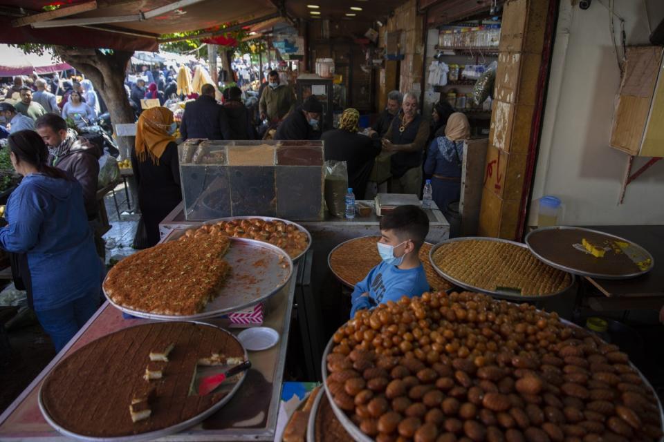 Large round trays filled with desserts cover tables at a crowded market.