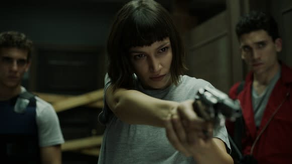 A woman pointing a gun at an unseen foe as two men look on in Netflix original La Casa de Papel (Money Heist).