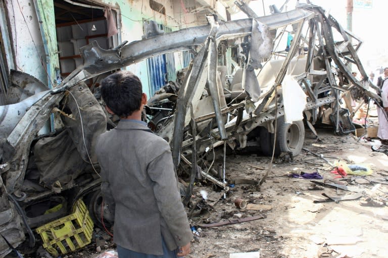 A Yemeni child stands next to the destroyed bus