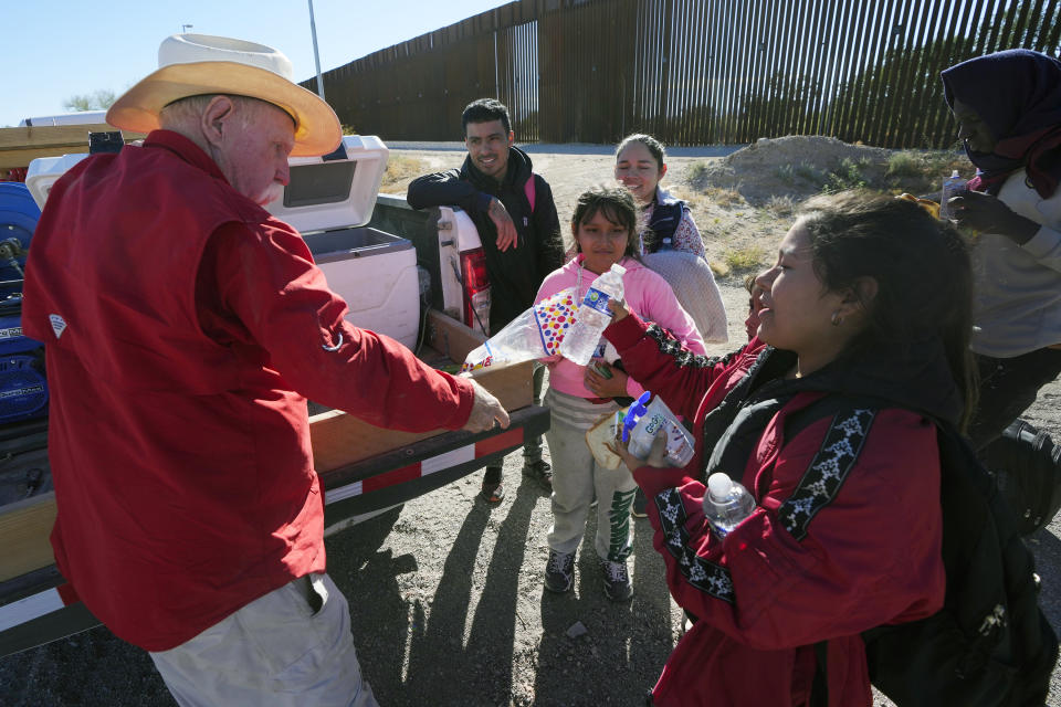 Tom Wingo, left, a humanitarian aid worker with Ajo Samaritans, hands out food and water to migrants gathered along the border including Gerston Miranda, second from left, and his family from Ecuador Tuesday, Dec. 5, 2023, in Lukeville, Ariz. (AP Photo/Ross D. Franklin)