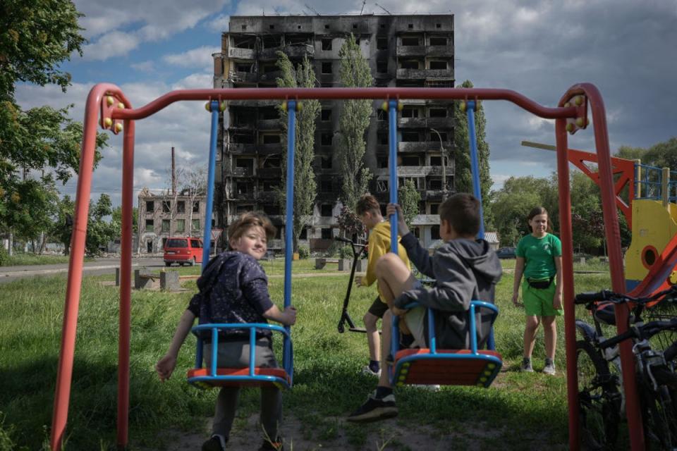 Children play on the swings outside a burnt-out building destroyed by a Russian missile strike in Borodyanka, Kyiv Oblast (Getty Images)