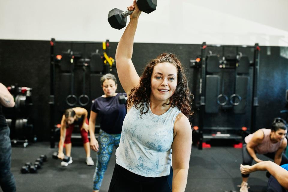 A woman lifting a dumbbell overhead in a fitness class.
