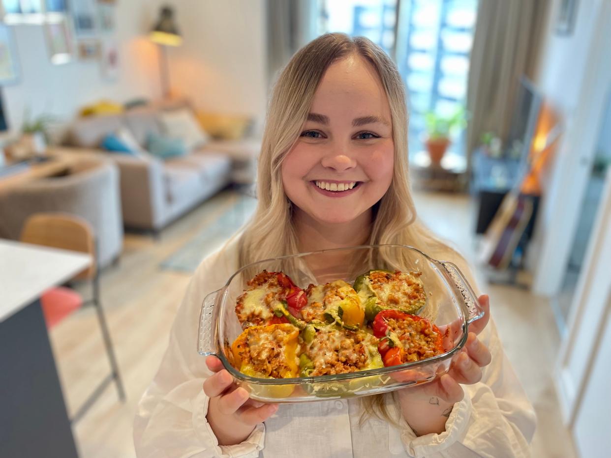 A woman holding a glass dish of stuffed peppers and smiling.