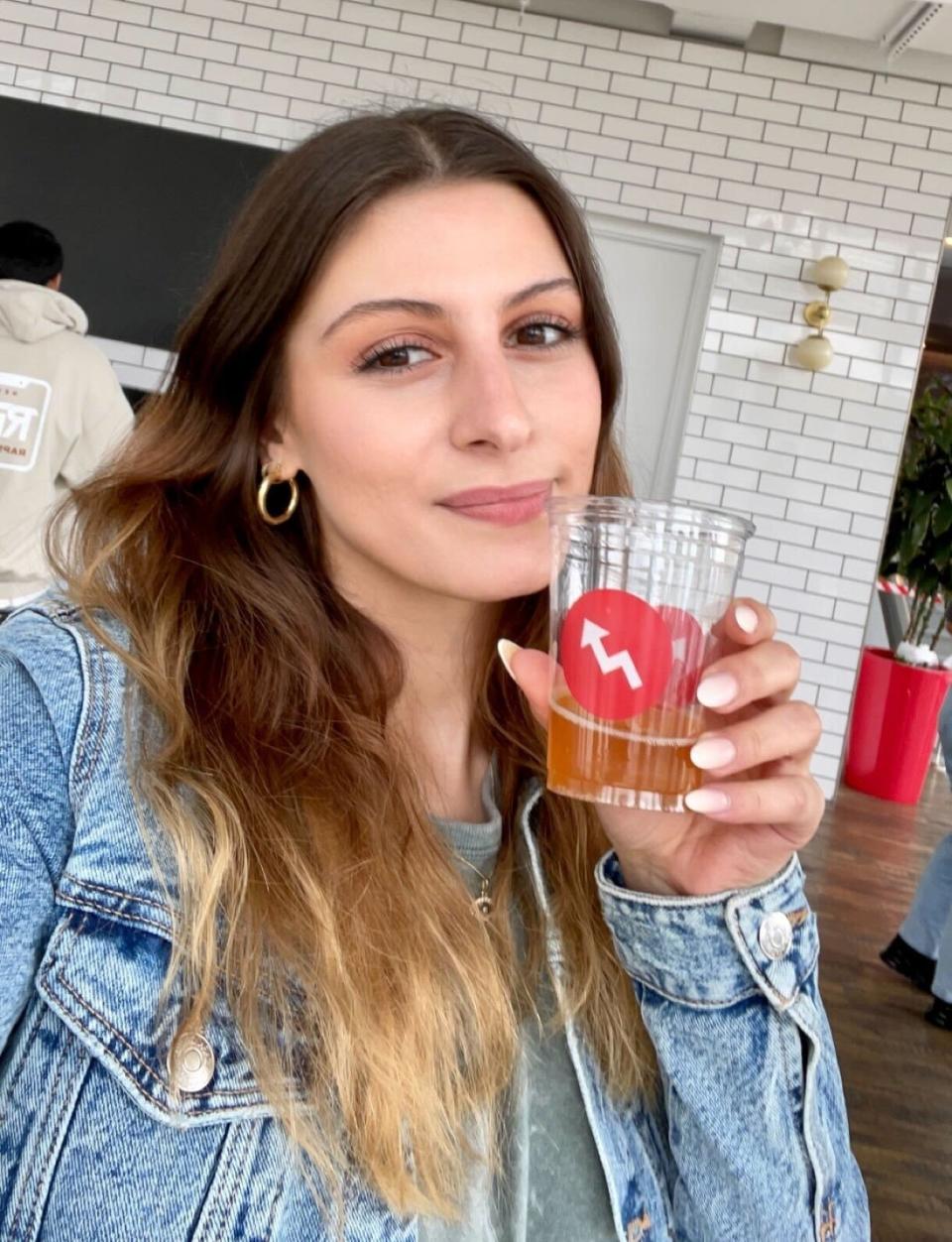 A woman wearing a denim jacket and holding a plastic cup containing a beverage