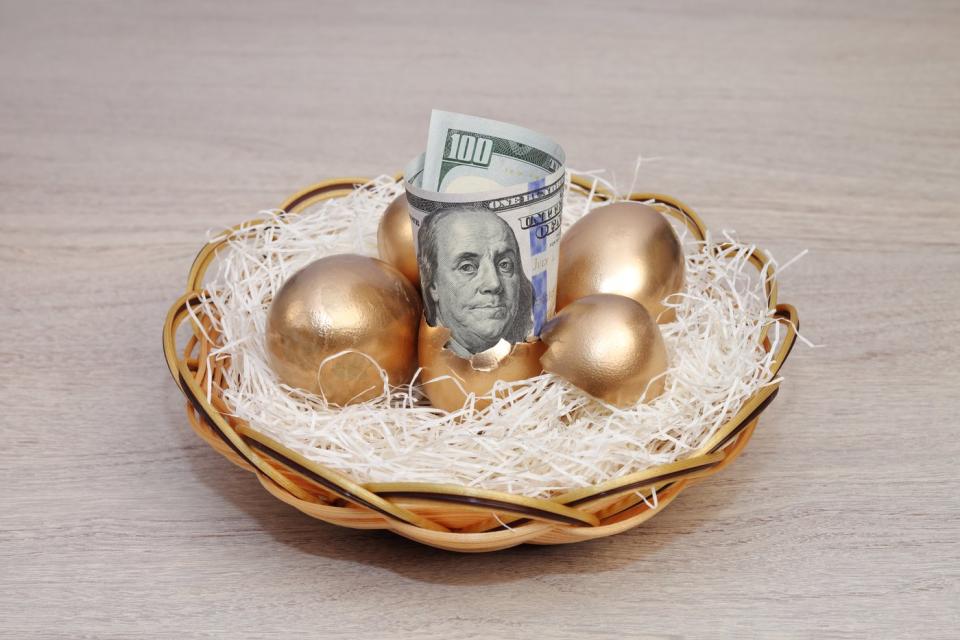 A hundred-dollar bill and several golden eggs in a bird's nest.