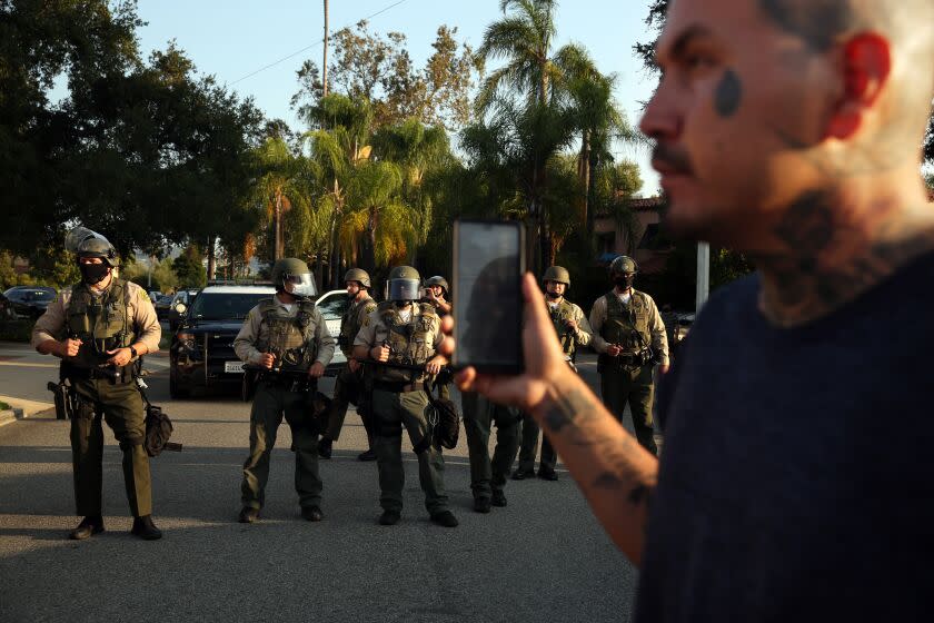 LOS ANGELES, CA - AUGUST 02: A person documents a line of sheriff's deputy's during a picket organized by the Coalition for Community Control Over the Police at the home of Los Angeles Sheriff's deputy Miguel Vega, who fatally shot Andres Guardado in Covina on Sunday, Aug. 2, 2020 in Los Angeles, CA. (Dania Maxwell / Los Angeles Times)