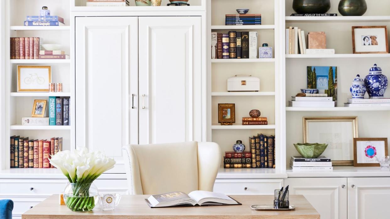  A whote home office with built in shelving and a wooden desk, books and trinkets adornding the shelves  