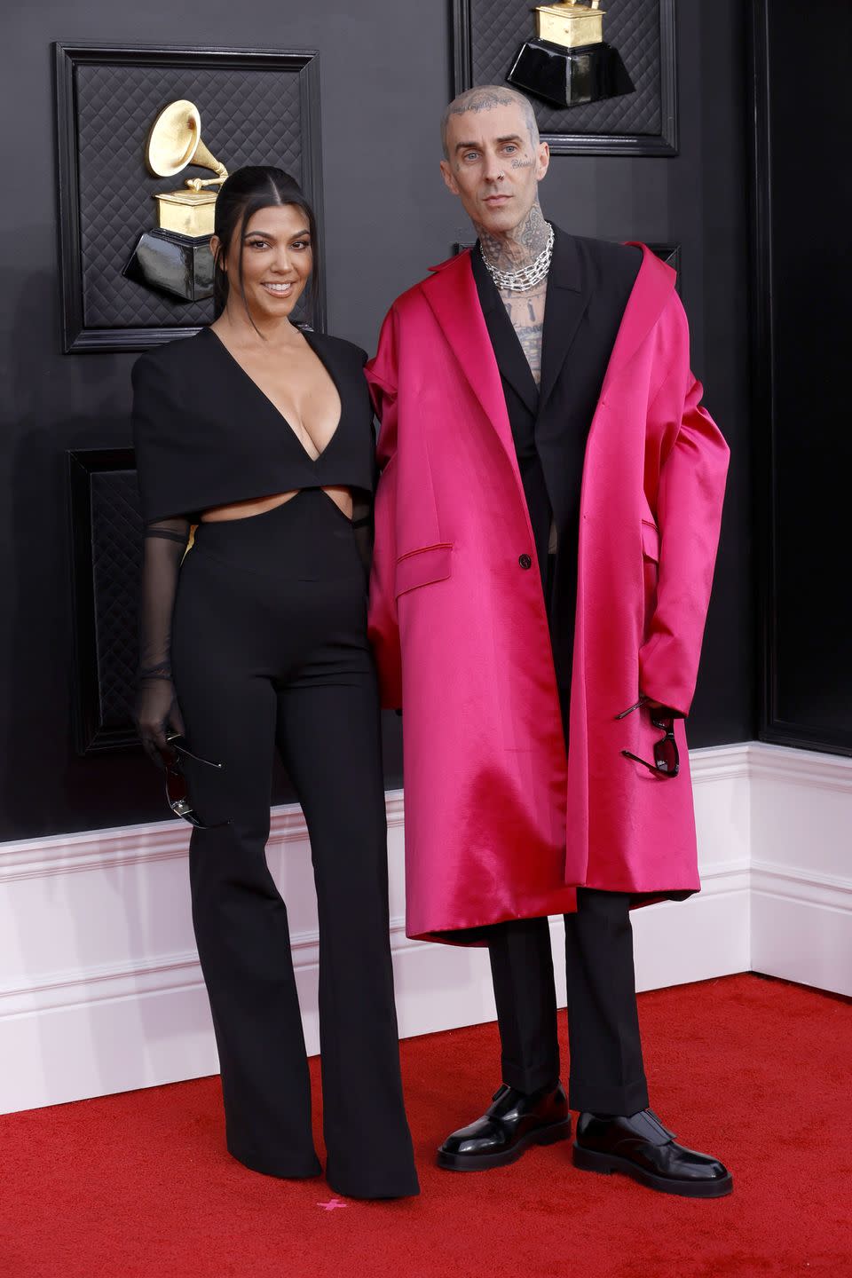 kourtney kardashian in a black trouser suit and travis barker in an oversized long pink jacket at the grammys